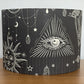 Black drum lampshade with white geometric and celestial designs on a dark grey background