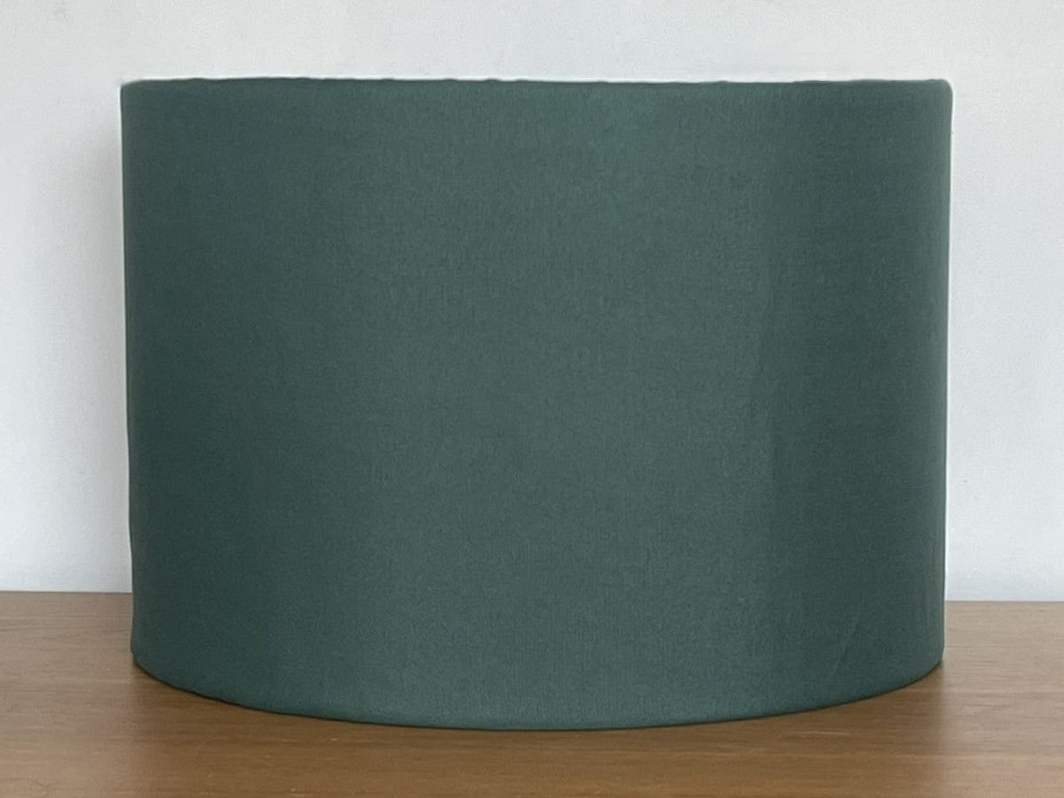 Green cylindrical lampshade on a wooden surface with a white background