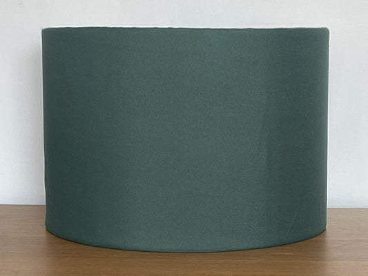 Green cylindrical lampshade on a wooden surface with a white background
