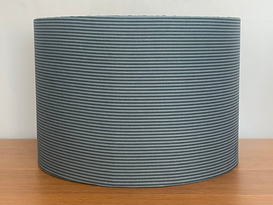 Blue striped fabric lampshade on a wooden surface with a white background