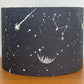 Black cylindrical lampshade with celestial designs on a wooden surface