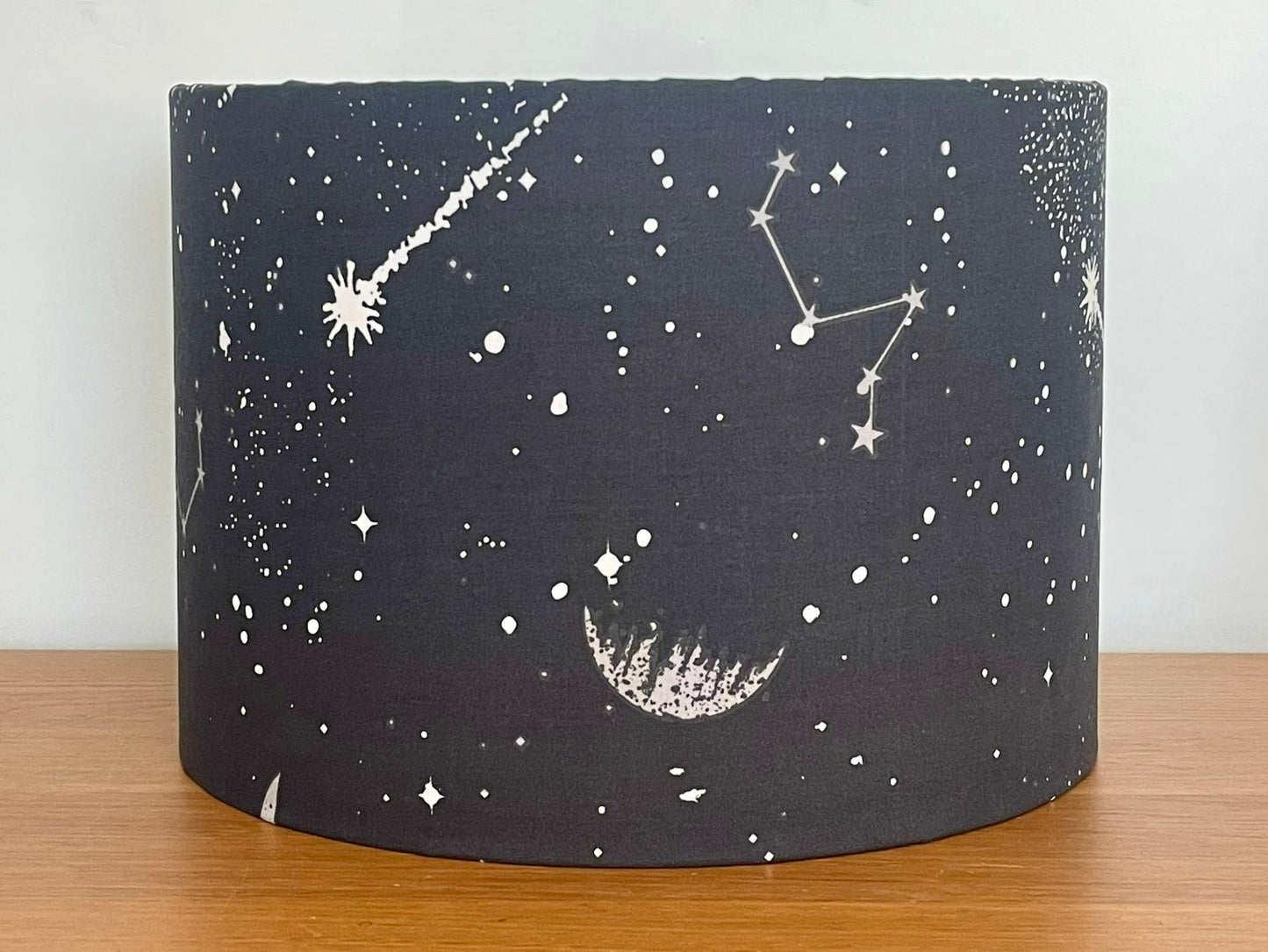 Black cylindrical lampshade with celestial designs on a wooden surface