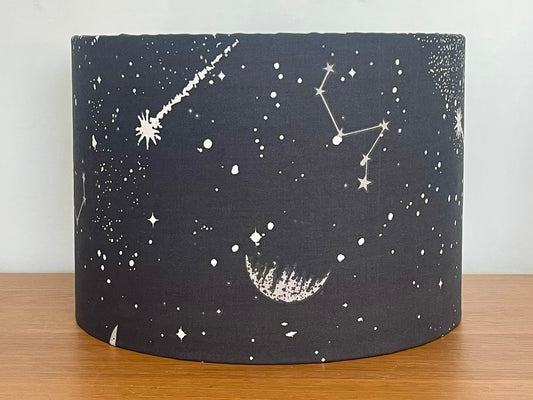 Black cylindrical lampshade with celestial designs on a wooden surface